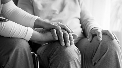 two people sitting with one leaning over to hold hands in a supportive gesture